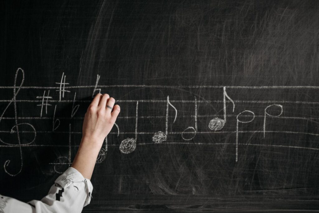 A person writing musical notes on a blackboard with chalk indoors.